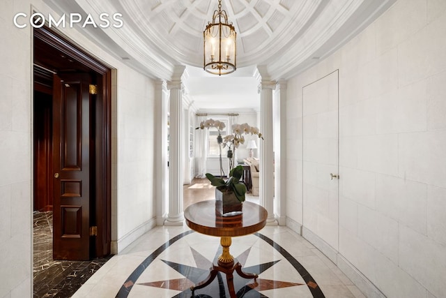 hall featuring ornate columns, crown molding, a raised ceiling, a notable chandelier, and tile walls