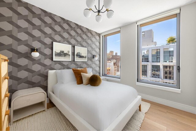 540 6th Ave Unit 11A, New York City, NY 10011 - bedroom featuring wallpapered walls, an accent wall, wood finished floors, a chandelier, and a view of city
