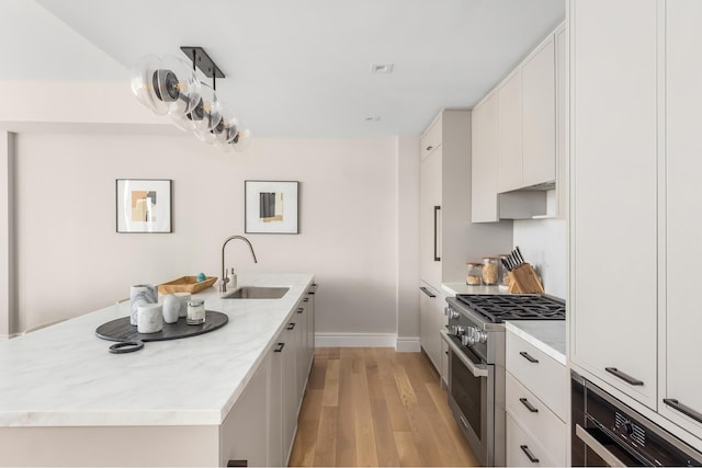 kitchen featuring high end stainless steel range oven, light wood-style flooring, white cabinetry, and a sink