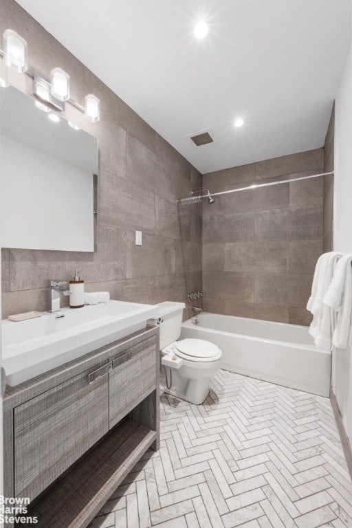 full bathroom with tile walls, toilet, vanity, and tiled shower / bath