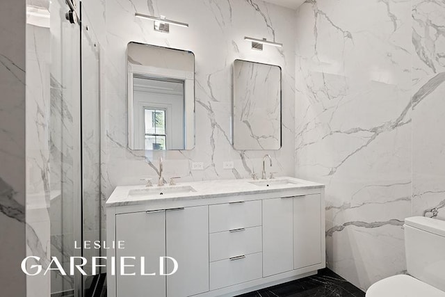 bathroom with toilet, marble finish floor, stone wall, and a sink