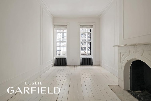 unfurnished living room with crown molding, radiator, light wood-style floors, and a decorative wall