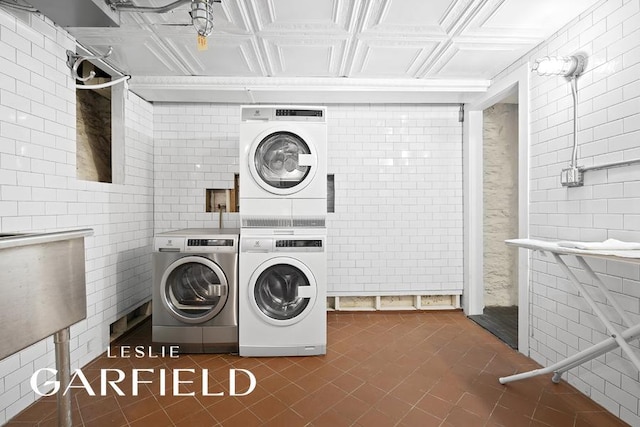 laundry room featuring stacked washer and dryer, an ornate ceiling, tile patterned flooring, washing machine and dryer, and tile walls