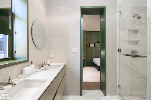 ensuite bathroom with marble finish floor, a sink, tile walls, and a shower stall