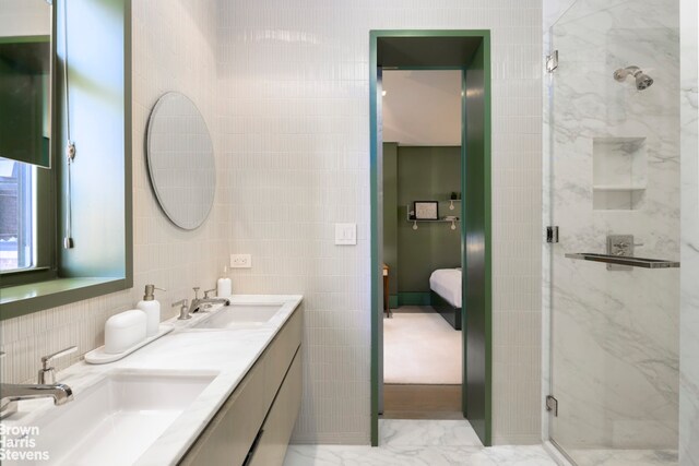 ensuite bathroom with tile walls, a marble finish shower, double vanity, and a sink