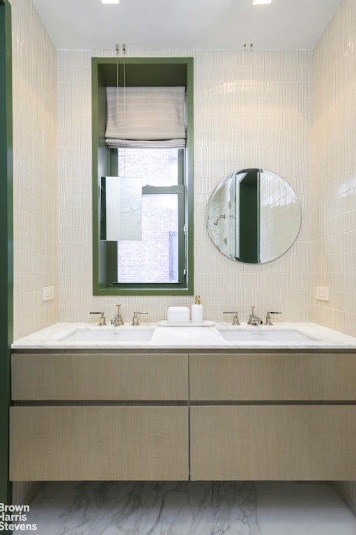 full bath with double vanity, a sink, and tile walls