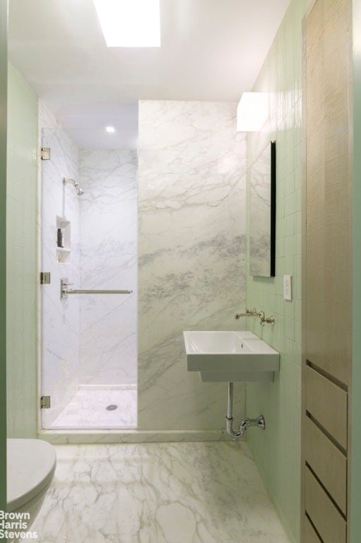 bathroom featuring a marble finish shower, tile walls, toilet, marble finish floor, and a sink