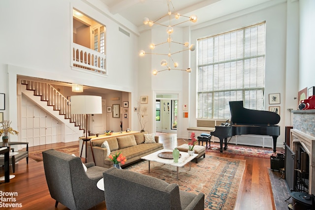 living room featuring stairway, wood finished floors, a fireplace, a towering ceiling, and an inviting chandelier