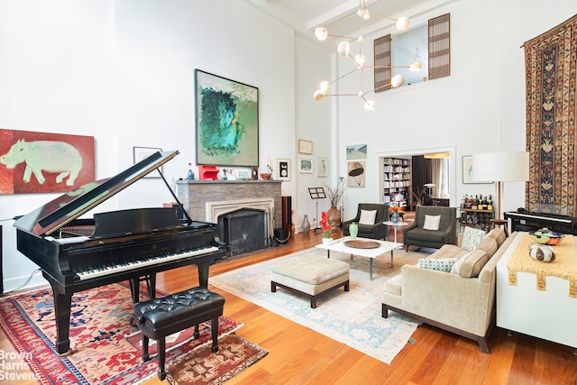 living area featuring wood finished floors, beam ceiling, a fireplace with raised hearth, a towering ceiling, and a notable chandelier