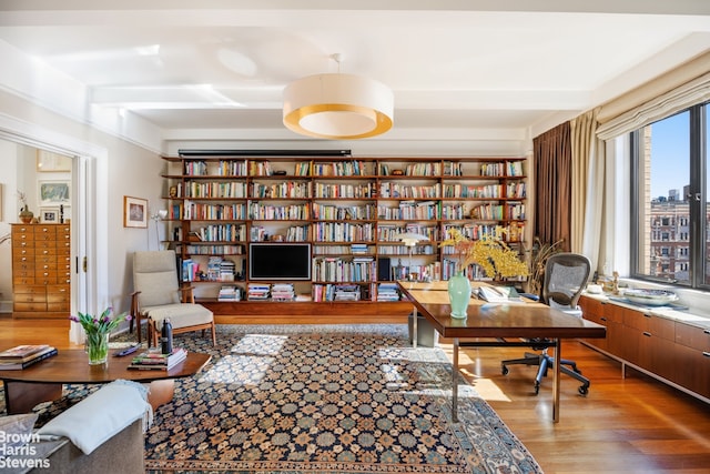 home office with beam ceiling, bookshelves, and wood finished floors