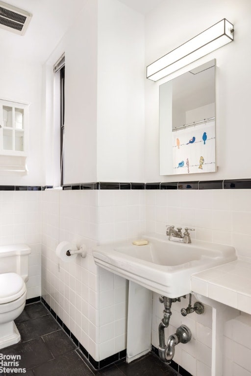 bathroom featuring visible vents, toilet, wainscoting, tile patterned floors, and tile walls