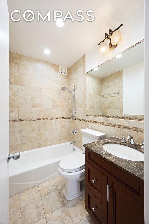 full bathroom with toilet,  shower combination, tile patterned flooring, vanity, and tile walls