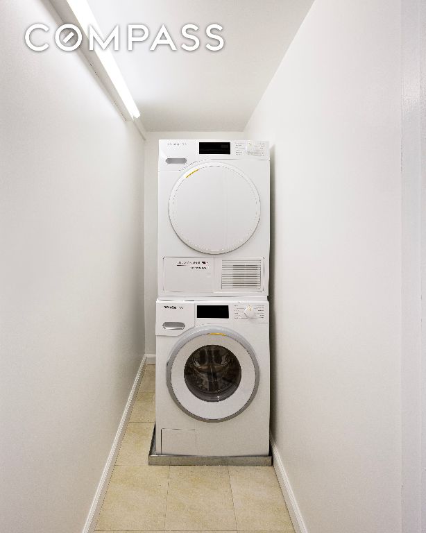 washroom with laundry area, light tile patterned floors, baseboards, and stacked washer / drying machine