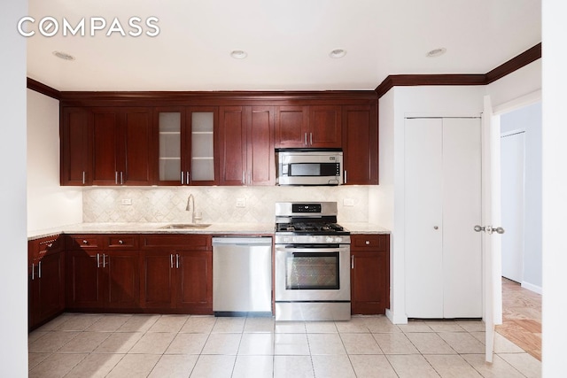 kitchen with light stone counters, stainless steel appliances, a sink, tasteful backsplash, and glass insert cabinets