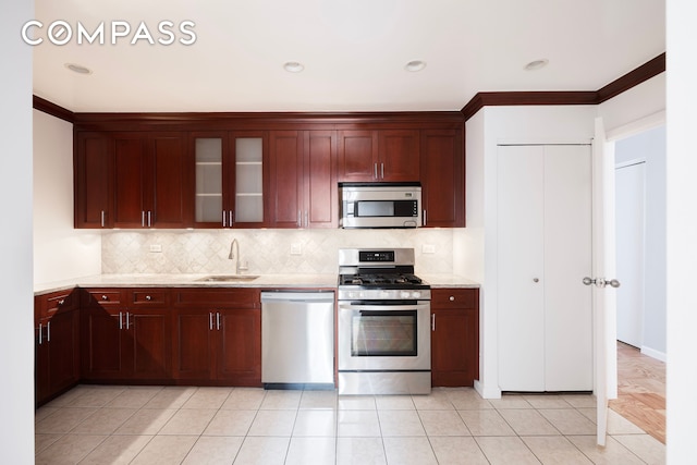 kitchen featuring decorative backsplash, a sink, stainless steel appliances, light tile patterned flooring, and glass insert cabinets