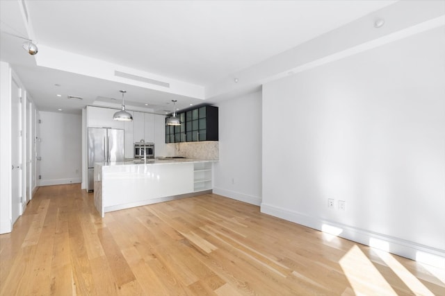 kitchen featuring tasteful backsplash, decorative light fixtures, kitchen peninsula, white cabinetry, and built in fridge