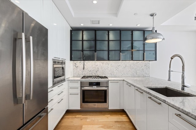 kitchen with light stone countertops, white cabinets, decorative light fixtures, stainless steel appliances, and sink