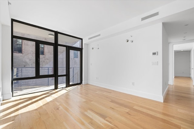 empty room with french doors, plenty of natural light, floor to ceiling windows, and light hardwood / wood-style floors