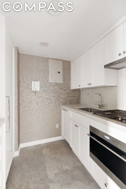 kitchen with oven, white cabinetry, sink, and electric panel