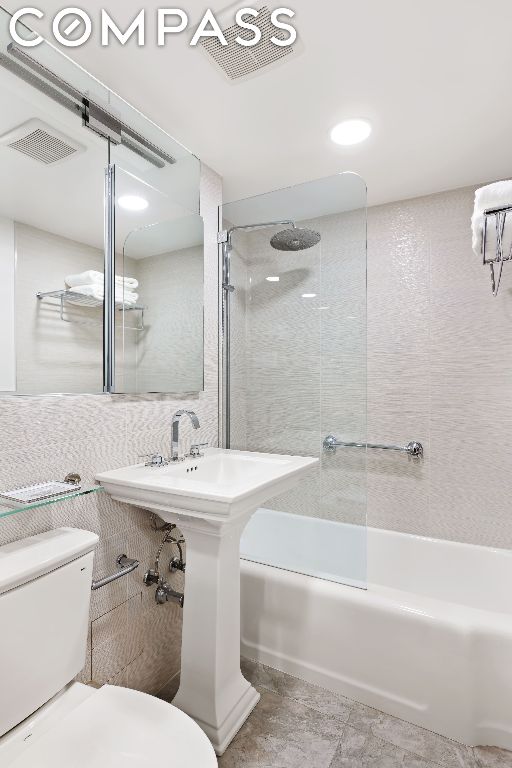 bathroom with toilet, tiled shower / bath combo, and tile walls