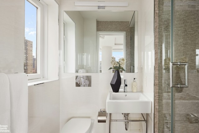 bathroom with sink, toilet, a shower with shower door, and a wealth of natural light