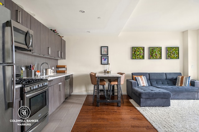 kitchen with decorative backsplash, appliances with stainless steel finishes, open floor plan, light countertops, and dark brown cabinets