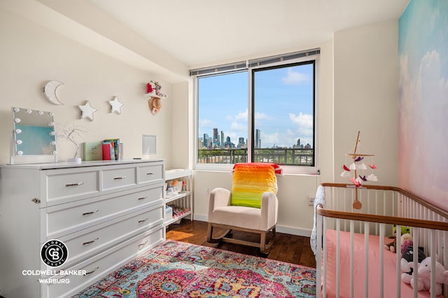 bedroom featuring a view of city, a crib, dark wood-style flooring, and baseboards