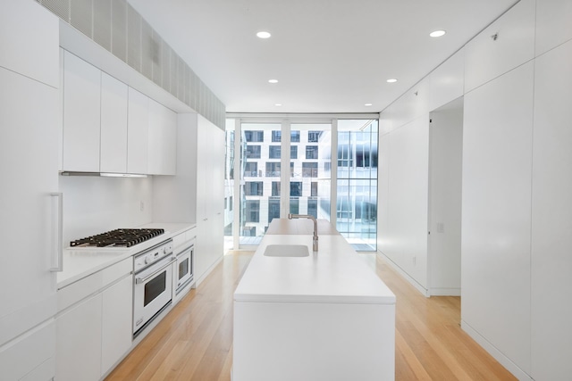 kitchen with gas stovetop, a sink, modern cabinets, a wall of windows, and oven