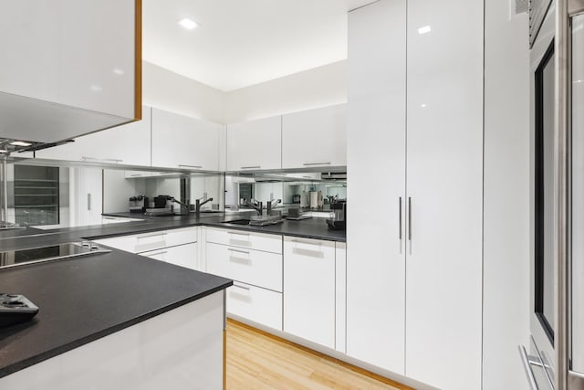 641 5th Ave Unit 27C, New York City, NY 10022 - kitchen featuring white cabinets, modern cabinets, dark countertops, electric stovetop, and light wood finished floors