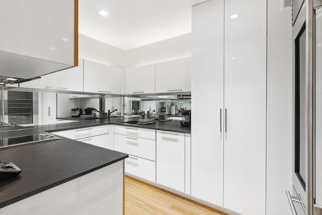 kitchen with light wood-type flooring, sink, black electric stovetop, and white cabinetry