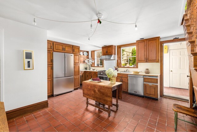 kitchen featuring brown cabinets, stainless steel appliances, light countertops, a sink, and under cabinet range hood