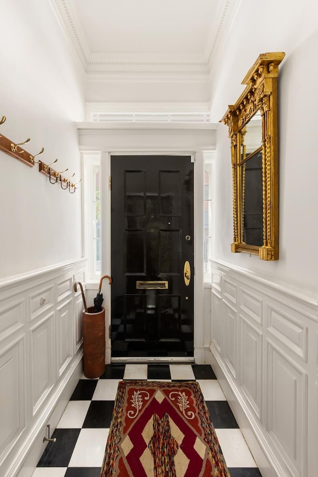 foyer entrance featuring light floors, ornamental molding, a decorative wall, and wainscoting