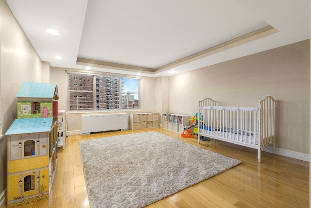 bedroom with baseboards, a raised ceiling, wood finished floors, and recessed lighting