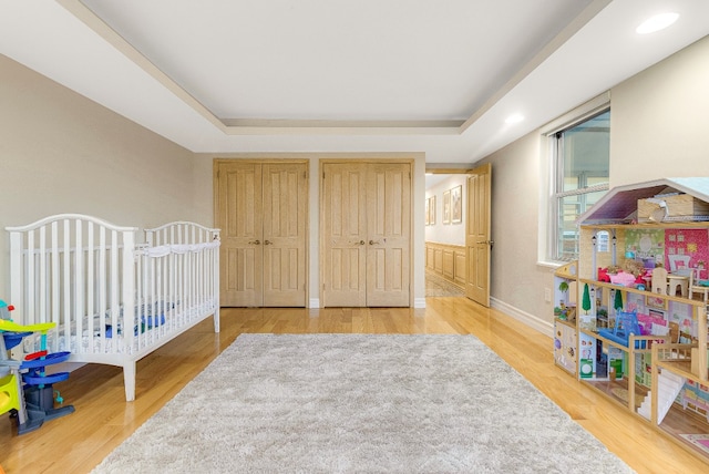 bedroom with two closets, a raised ceiling, and wood finished floors