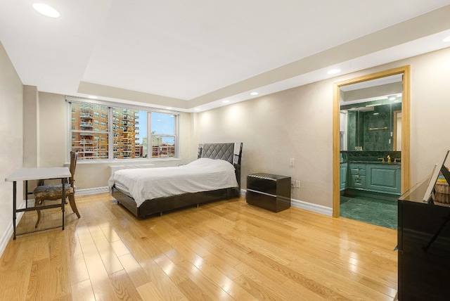 bedroom with ensuite bath, wood-type flooring, and a raised ceiling