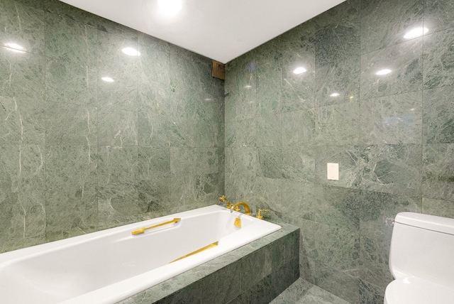 bathroom with tile walls, tiled bath, and toilet