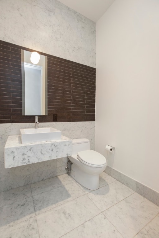 half bath with toilet, a sink, baseboards, and tile walls