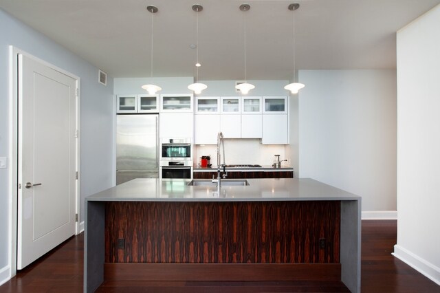 243 W 60th St Unit 3A, New York City, NY 10023 - kitchen with appliances with stainless steel finishes, white cabinetry, a large island with sink, dark wood-style floors, and light countertops