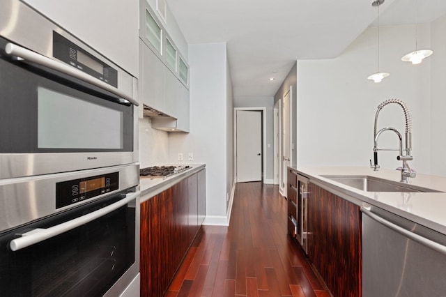 kitchen with appliances with stainless steel finishes, dark hardwood / wood-style floors, decorative light fixtures, white cabinets, and sink