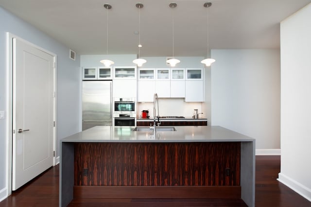 kitchen with hanging light fixtures, white cabinets, an island with sink, and stainless steel appliances