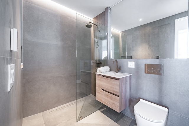 bathroom with tile patterned flooring, vanity, tile walls, toilet, and a tile shower