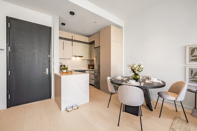 kitchen with tasteful backsplash, light wood-type flooring, stainless steel refrigerator, and cream cabinets