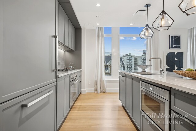 kitchen with sink, gray cabinetry, hanging light fixtures, light wood-type flooring, and light stone countertops