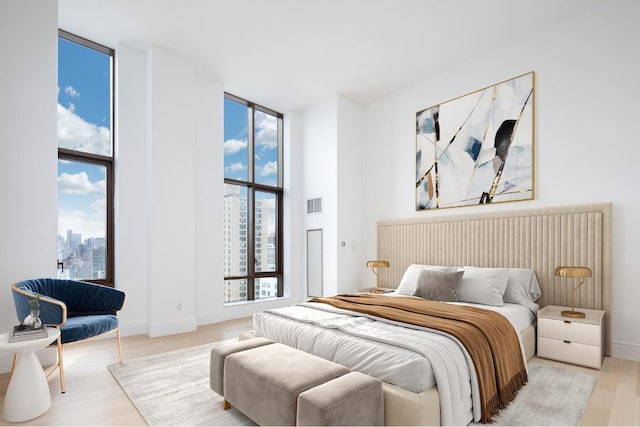 bedroom featuring a view of city, light wood finished floors, visible vents, a wall of windows, and baseboards