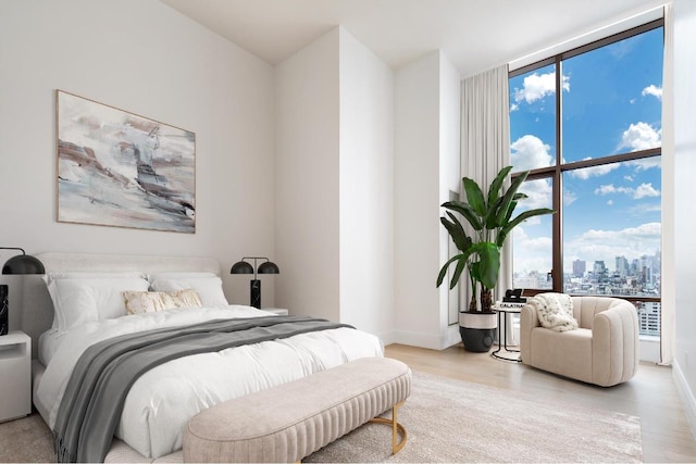 bedroom featuring a wall of windows, a city view, light wood-style flooring, and baseboards