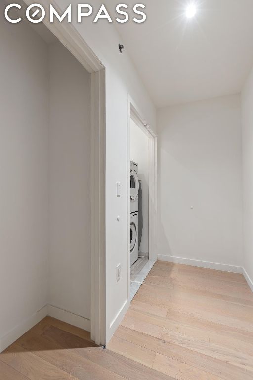 clothes washing area with hardwood / wood-style flooring and stacked washer / dryer