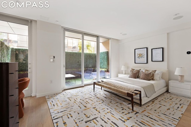 bedroom featuring light wood-type flooring, access to exterior, and floor to ceiling windows