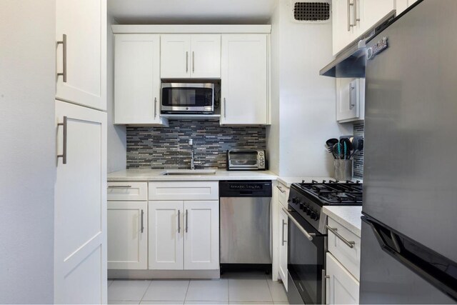 kitchen featuring backsplash, sink, light tile patterned floors, appliances with stainless steel finishes, and white cabinets