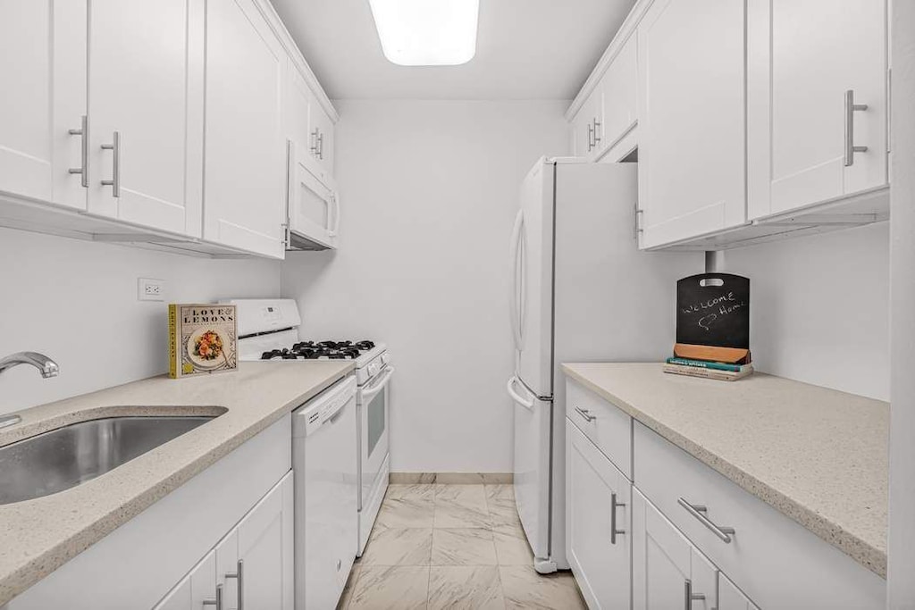 kitchen with white cabinetry, white appliances, light stone countertops, and sink