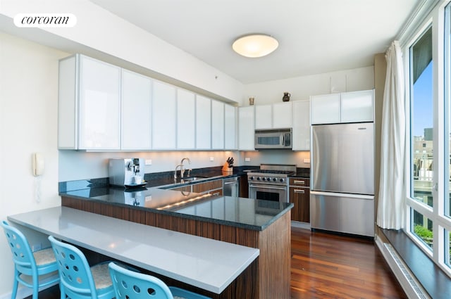 kitchen with appliances with stainless steel finishes, a breakfast bar area, white cabinets, kitchen peninsula, and dark wood-type flooring